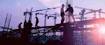 Silhouettes of construction workers are seen on a building site at sunset. Several cranes are in the background against a sky with pink and blue hues, highlighting the ongoing construction activity. The sun rays add a warm glow to the scene.