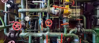 A complex network of green pipes, valves, and gauges in an industrial setting with numerous red-handled controls and a yellow tank. The pipes are interconnected in various configurations, indicating a possibly large and intricate system.