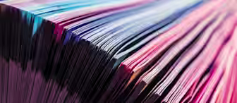 Close-up of a book with colorful pages fanned out. The edges of the pages display a spectrum of vibrant colors ranging from pink to blue, creating a striking and visually appealing pattern.