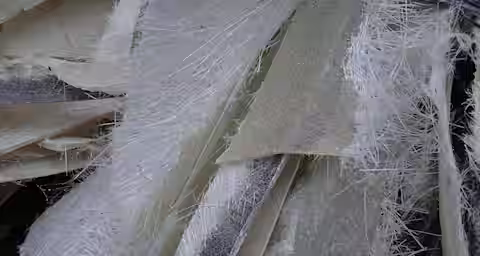 Close-up image showing a chaotic arrangement of translucent fiberglass strands and sheets. The material appears uneven and frayed at the edges, displaying a mix of coarse fibers and smooth surfaces.