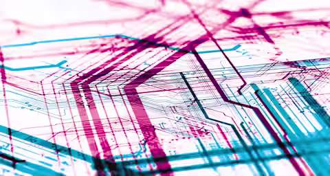 Abstract image of a complex circuit board design with overlapping red and blue lines, illustrating the intricate pathways and connections of an electronic system. The image emphasizes the detailed and layered structure of the circuitry.