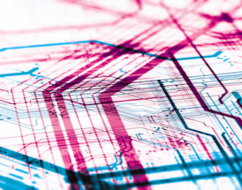 Abstract image of a complex circuit board design with overlapping red and blue lines, illustrating the intricate pathways and connections of an electronic system. The image emphasizes the detailed and layered structure of the circuitry.