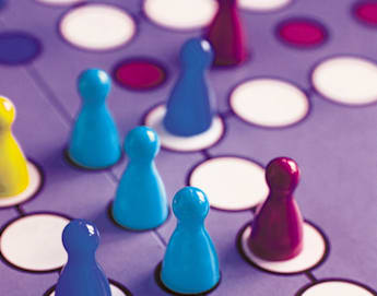 A close-up of a colorful board game with blue and purple game pieces arranged on interconnected circles. One blue piece is lying on its side, indicating active gameplay. The background features a purple board with white circles connected by lines.