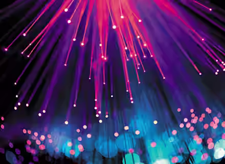 A display of colorful fiber optic lights emanating outward, creating streaks and points of vibrant pink, purple, and blue against a dark background. The lower part of the image features a bokeh effect with blue and pink glowing circles.