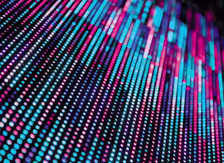 A dynamic pattern of blue, pink, and purple vertical lines in various lengths against a dark background, resembling LED light strips. The lights blur towards the top, creating a vibrant, abstract visual effect.