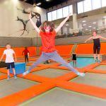 child in orange T-shirt jumpimg and smiling on a large trampoline