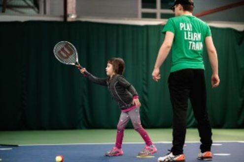 Little girl playing tennis with instructor
