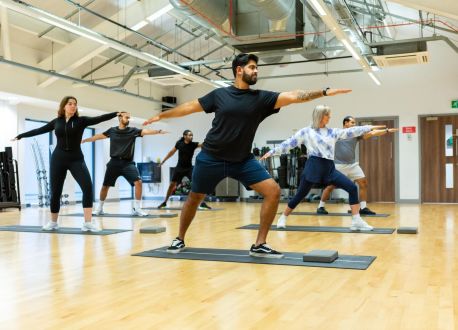 class of adults doing yoga standing with arms outstretched