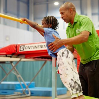 A young gymnast being assisted on bars by a coach