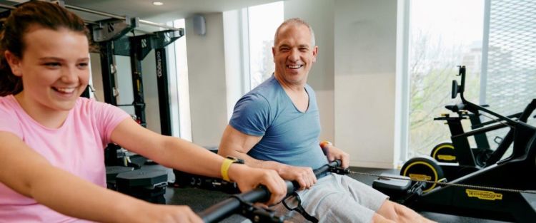 Image shows a dad and his daughter working out in the gym on the rowing machines together