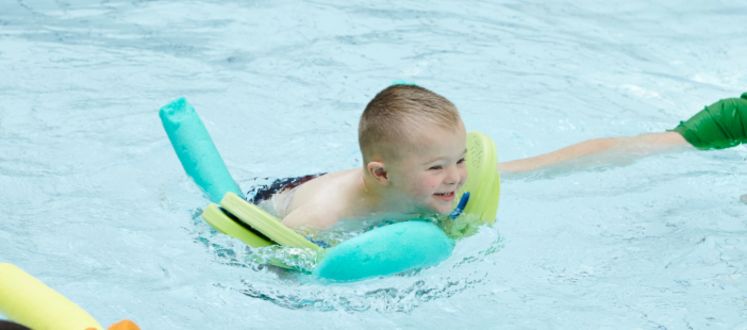 young boy swimming with pool noodle