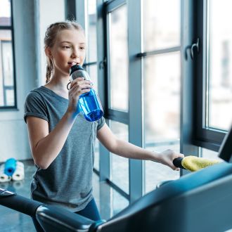 image shows a pre-teen girl on a treadmill drinking water.