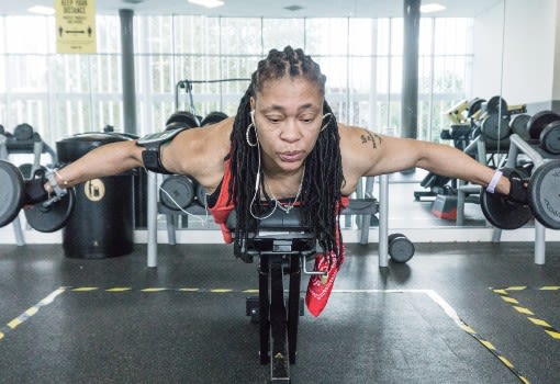 Female in the gym lifting two dumbbells with headphones in