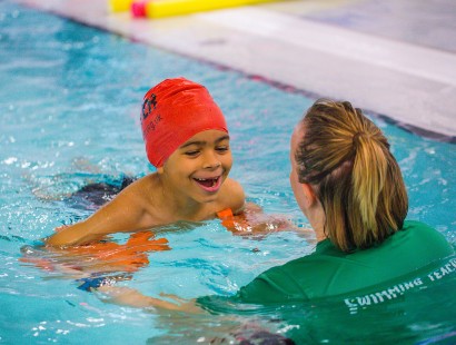 Little boy learning to swim in a swimming pool with a teacher