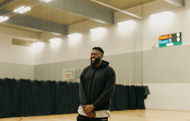 Manwith black hoodie standing smiling in a basketball court