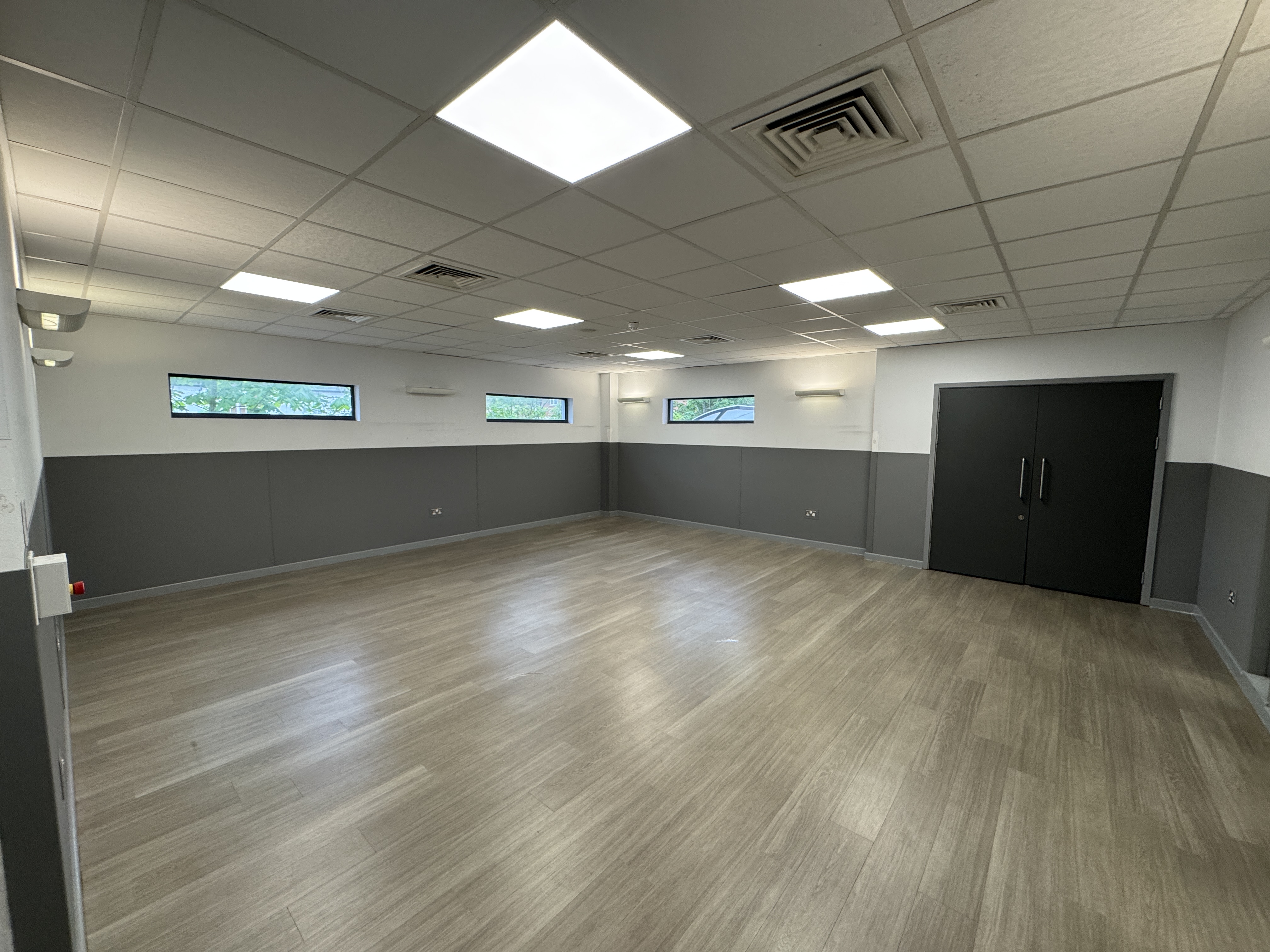 Spacious activity room with wood-effect flooring, grey and white walls, ceiling lights, and double doors at Southgate Leisure Centre.