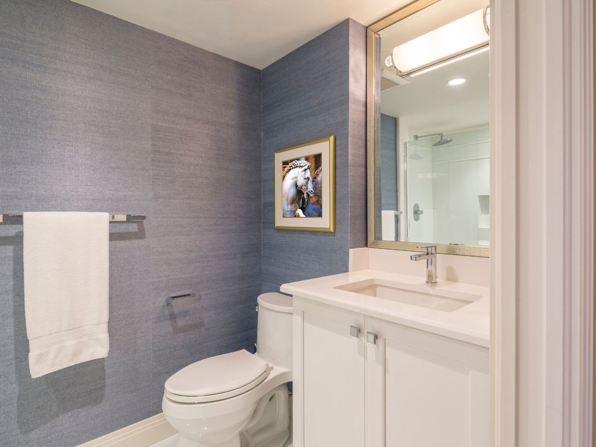 Ein schlichtes Gäste-WC mit blau tapezierter Wand, weißem Waschtisch und einem gerahmten Bild, das einen stilvollen Akzent setzt und den Raum persönlich und einladend macht.