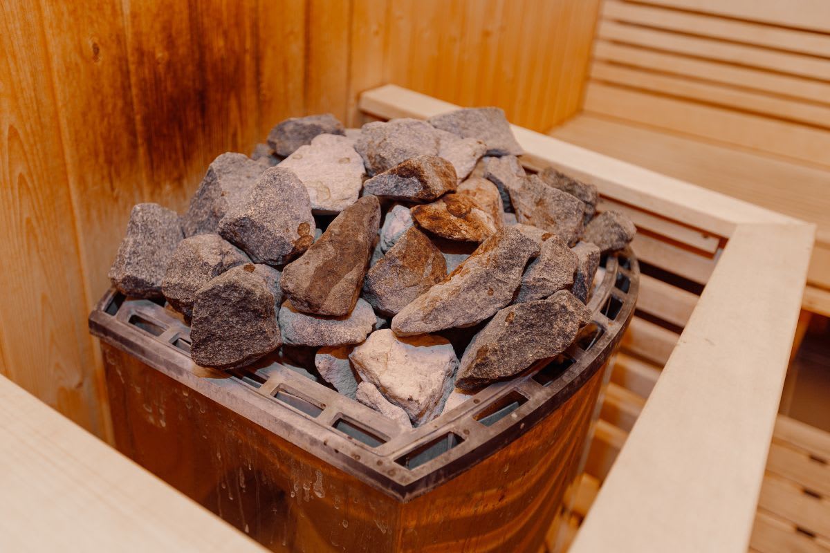 Ein traditioneller Saunaofen gefüllt mit grauen Saunasteinen innerhalb einer Holzsauna.