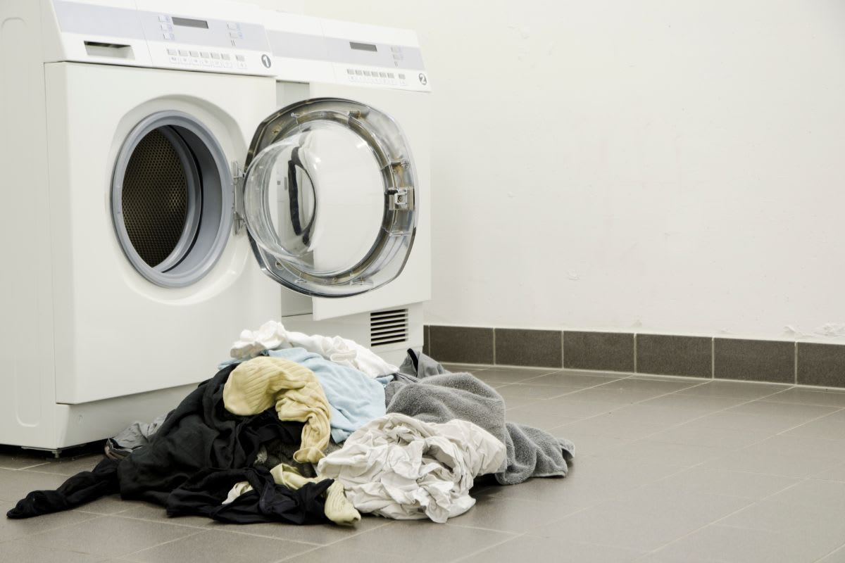 Unordentlicher Haufen von Kleidung auf dem Boden vor einer geschlossenen Waschmaschinentür.
