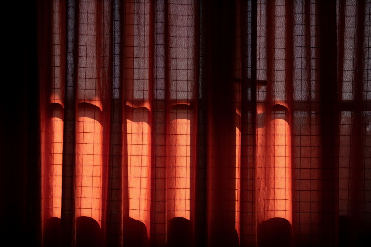 Roter Stoffvorhang, der Sonnenlicht filtert und einen warmen, gemütlichen Schimmer im Raum erzeugt.