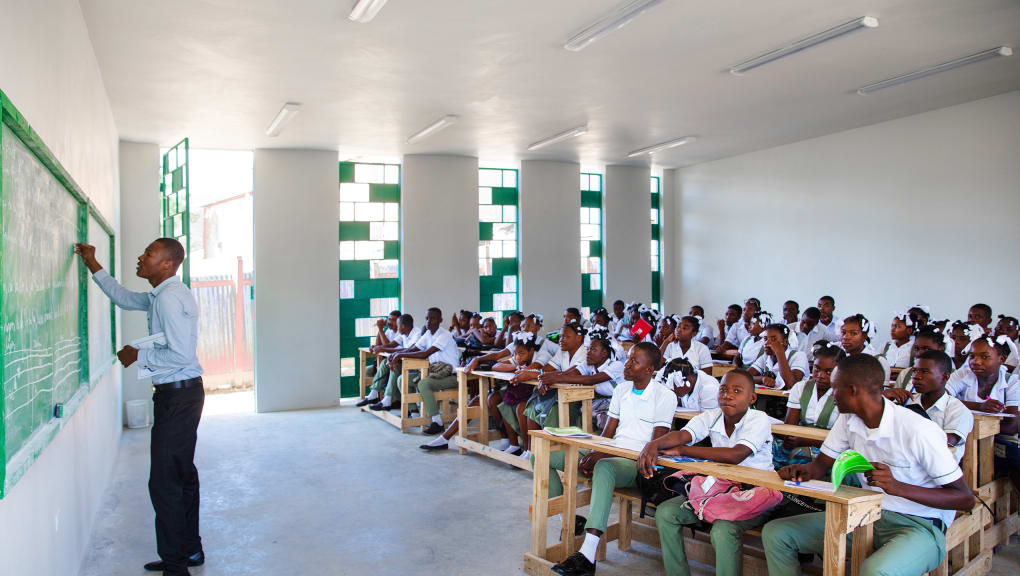 Teacher writing on a blackboard in front of a class of children at La Reference