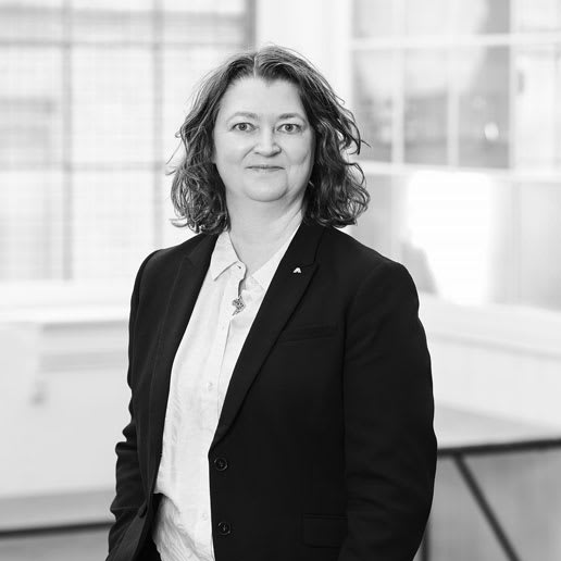 A black and white portrait of a woman with shoulder-length wavy hair, wearing a blazer over a collared shirt.