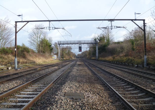 Exterior ground level view in-between rail tracks of the Elizabeth Line gantry