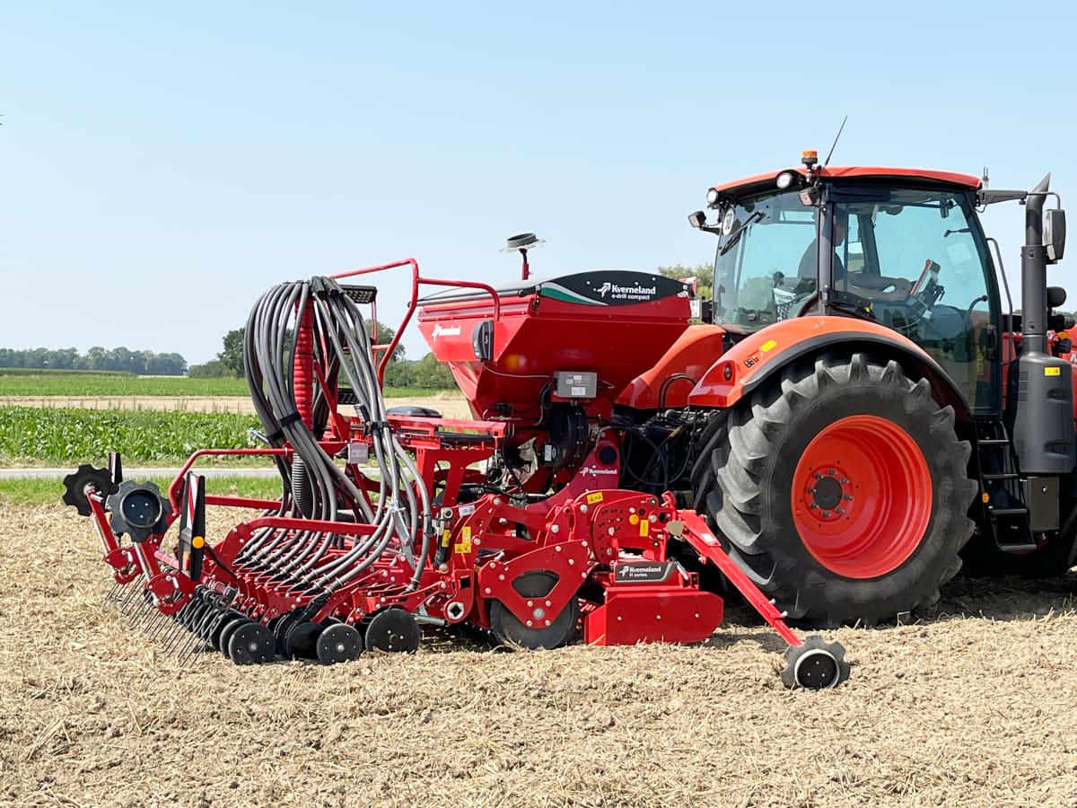 Red Kverneland seed drill combination hitched to a tractor in a field, showing the hopper, seed distribution system, and coulters ready for precision seeding.
