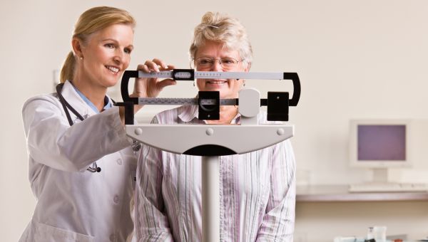 woman standing on a scale being weight by doctor