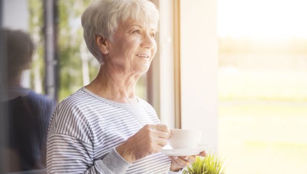 woman standing at a sunny window with a cup of coffee tea