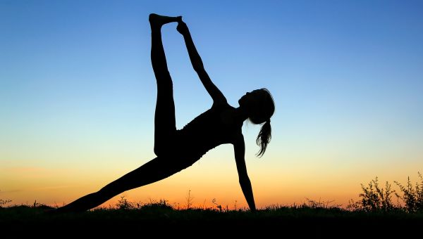 woman doing yoga outdoors as sun sets - blue to yellow sky