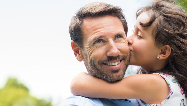 Portrait of a little girl kissing her dad on cheek. Pretty girl giving a kiss to her father outdoor. Loving child embrace and kissing her father.