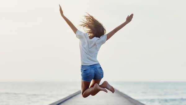 Photo showing back of someone jumping in front of the ocean