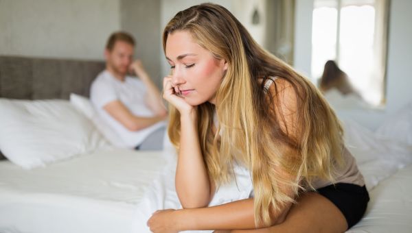 two pensive people sitting in bed, with one person facing away from the other one