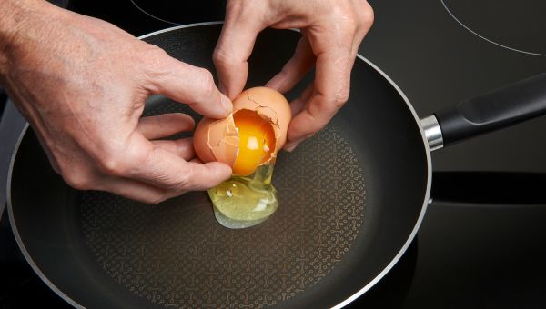 man cracking egg over frying pan