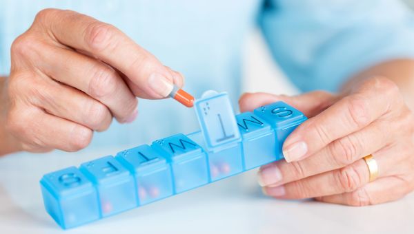 woman placing pill into daily pill container