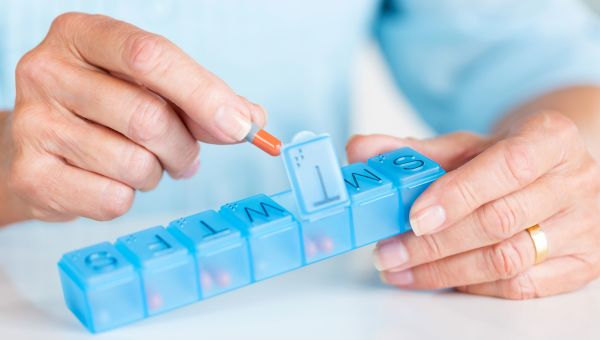 woman placing pill into daily pill container