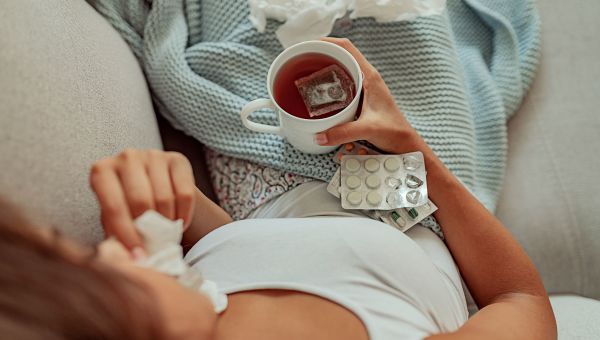 Woman with a cold drinking hot tea and taking cold medicine