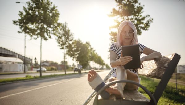 woman with glasses on park bench with broken foot cast