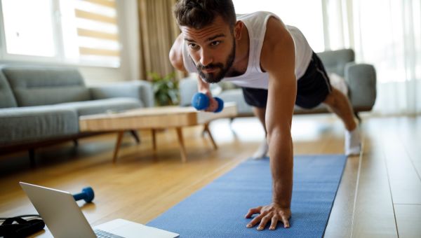 man lifting weight on mat in front of laptop