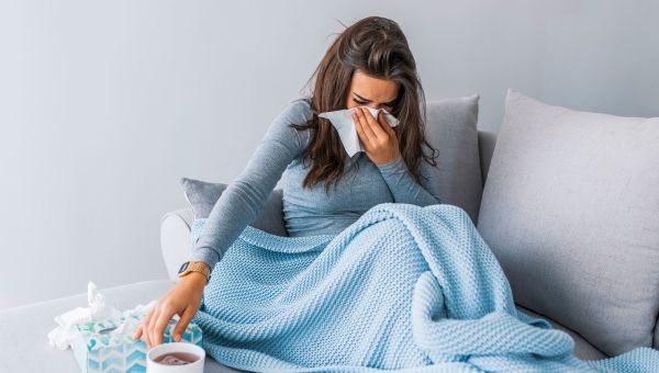 A woman blowing her nose on the couch with a cold