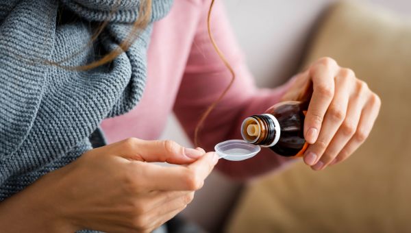 A woman measuring out cough syrup to help battle her cold.