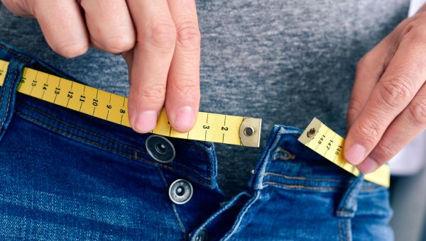 Person measures waist with tape measure.