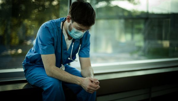 a tired male nurse sits and collects his thoughts in front of a large window