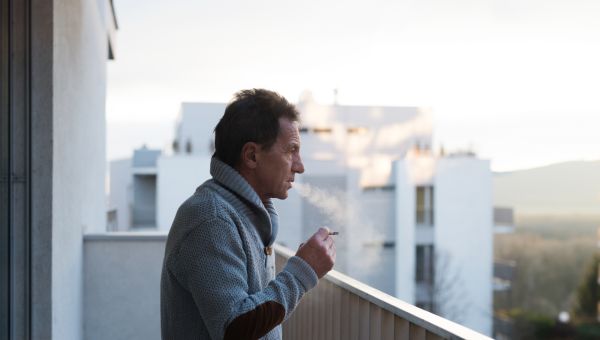 middle aged man smokes a cigarette on a balcony