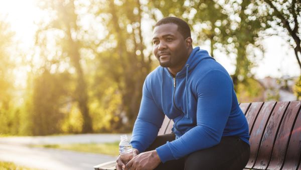 a fit but overweight Black man sits on a park bench after exercising