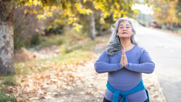 Older woman with long gray hair, doing a yoga namaste pose with their hands.
