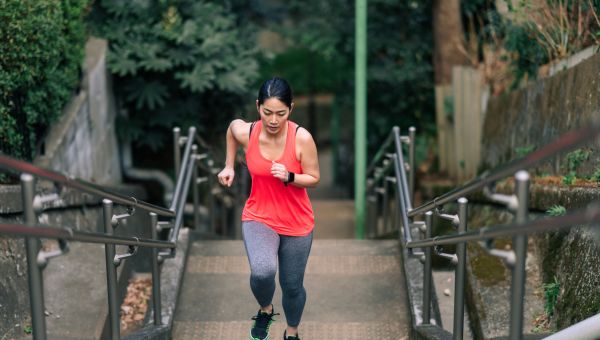 Asian American woman exercising outside, running up a flight of stairs