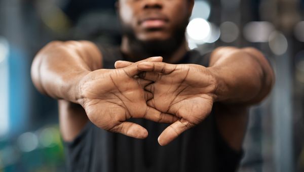 Muscular man in a gym stretching out his arms with his palms facing forward.