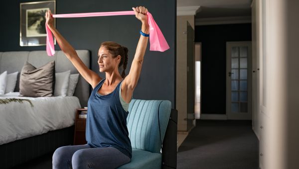 A woman with armbands doing an at-home workout on a chair in her bedroom.